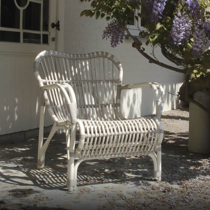 A white aluminium and weave outdoor chair surrounded by vibrant flowers and foliage, providing a charming seating area in a tranquil garden setting.